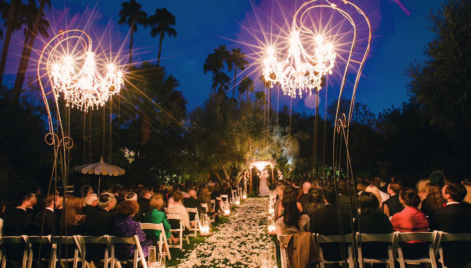 A beautiful outdoor wedding ceremony in a garden with blooming flowers and guests seated on white chairs.