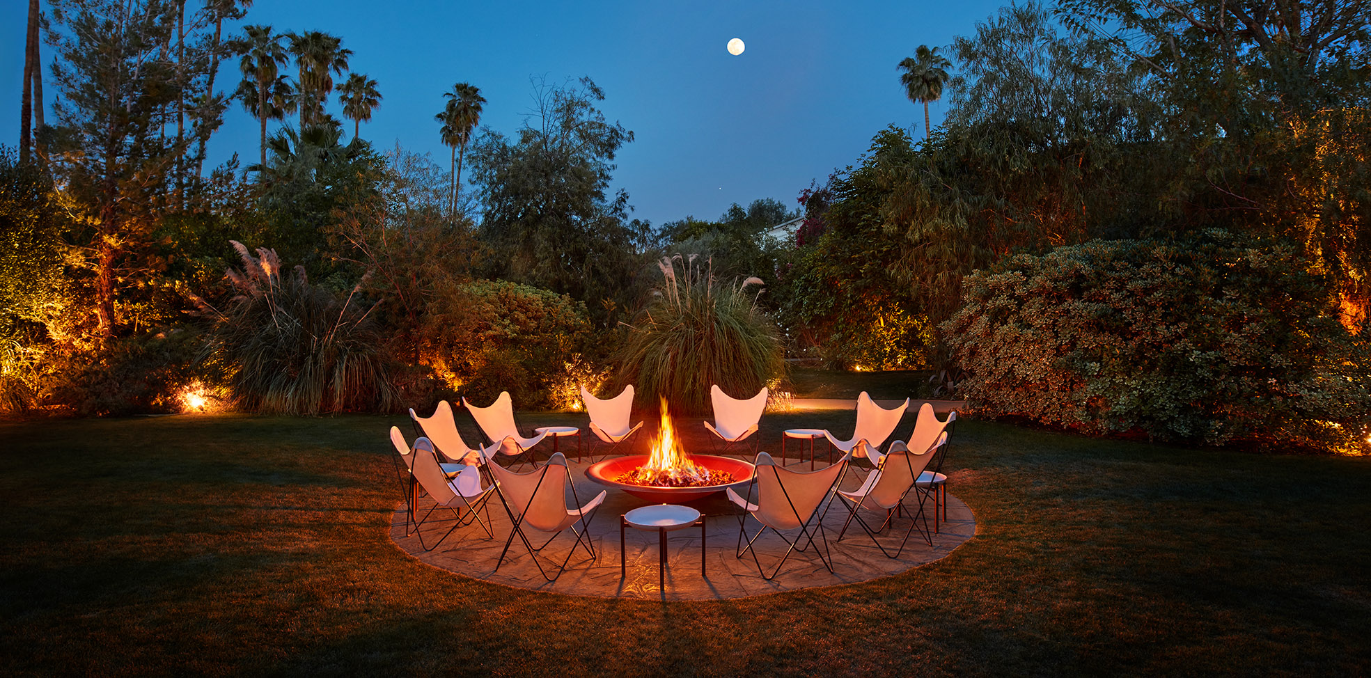 firepit at night in joshua tree with white chairs and tables surrounding