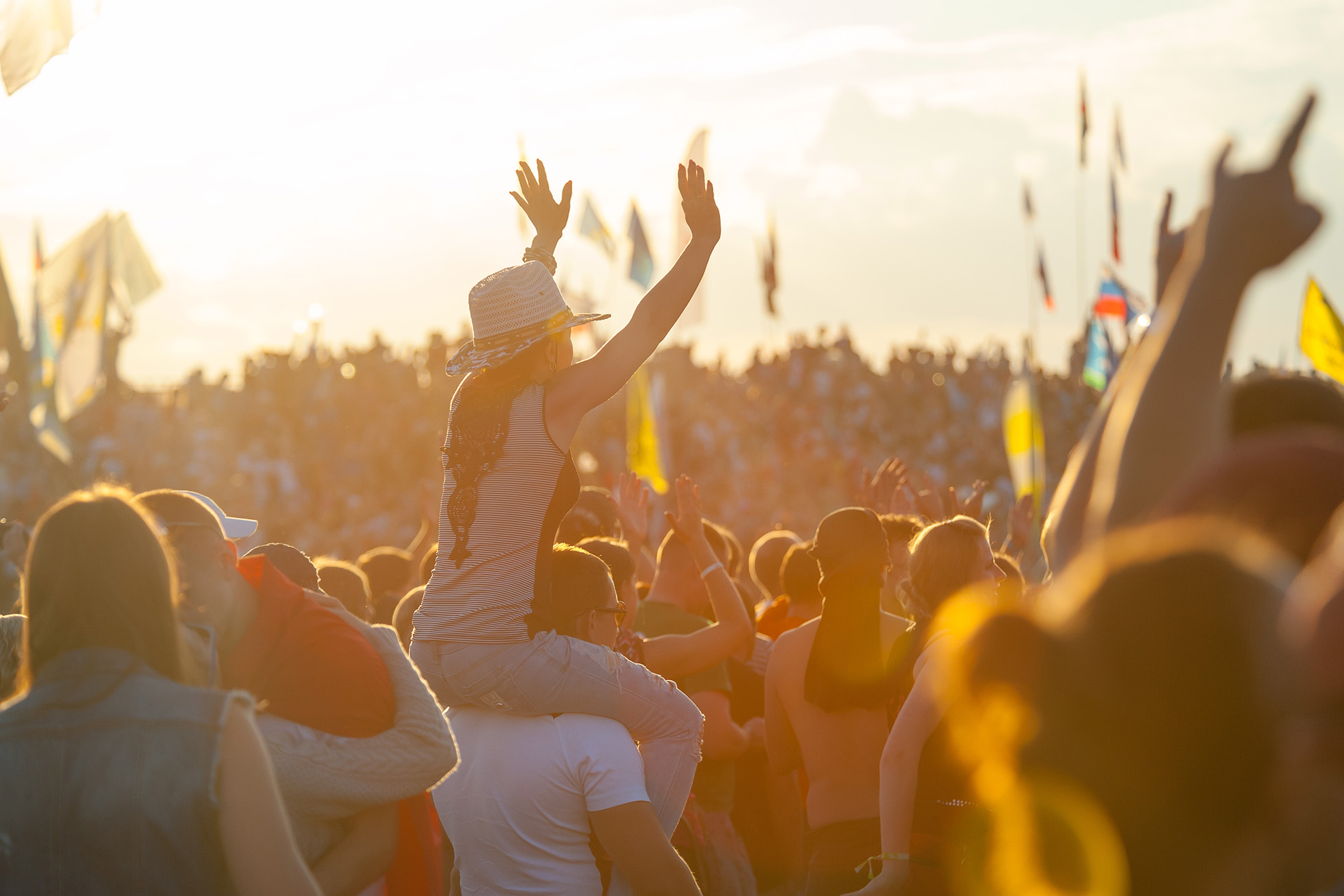 woman on shoulders of friend at concert waving her hands in the air