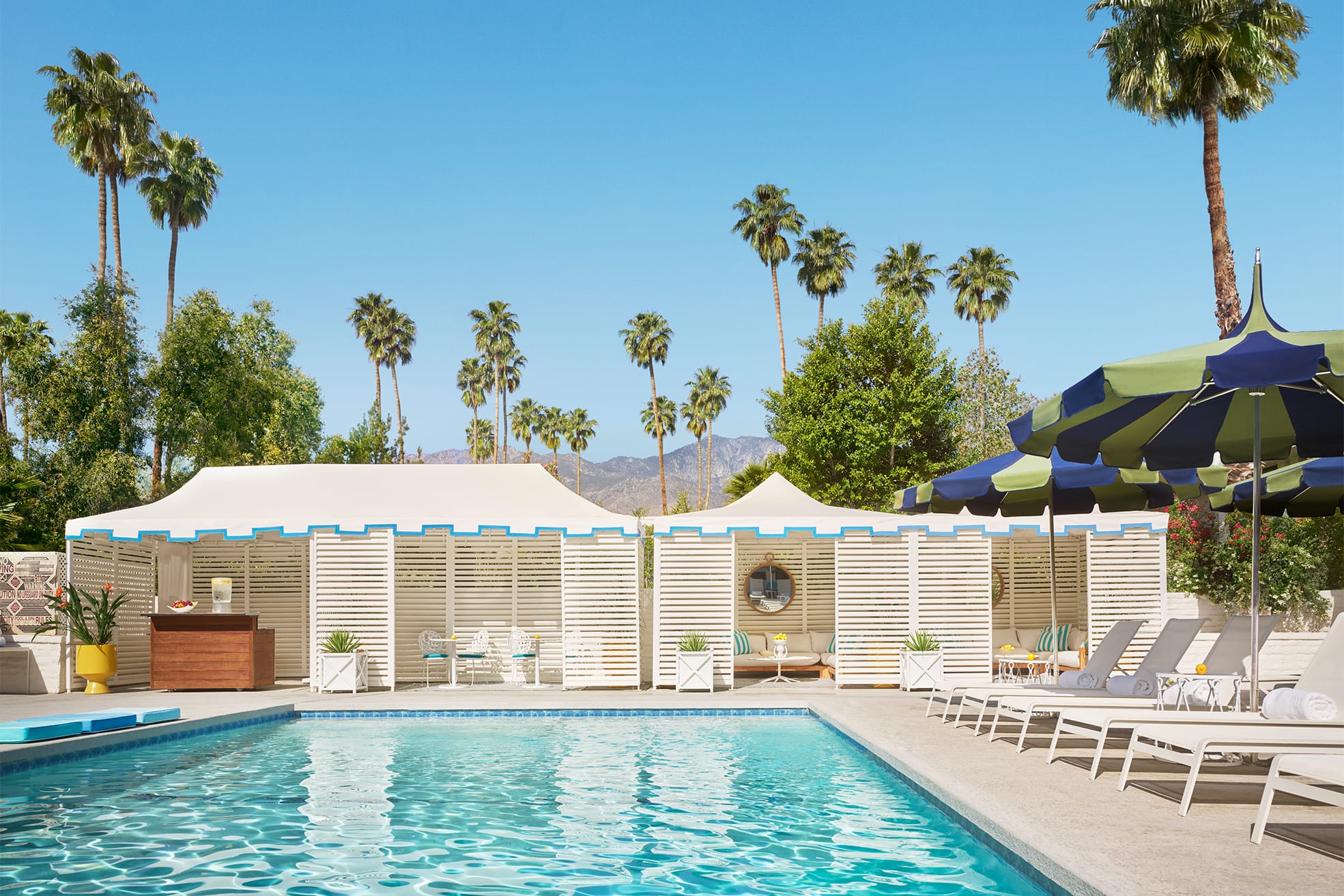 outdoor pool with lounge seating, cabanas, and palm trees